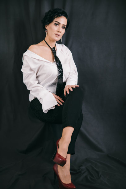 年轻自信的女人坐在工作室的椅子上，黑色背景，白色衬衫图片下载