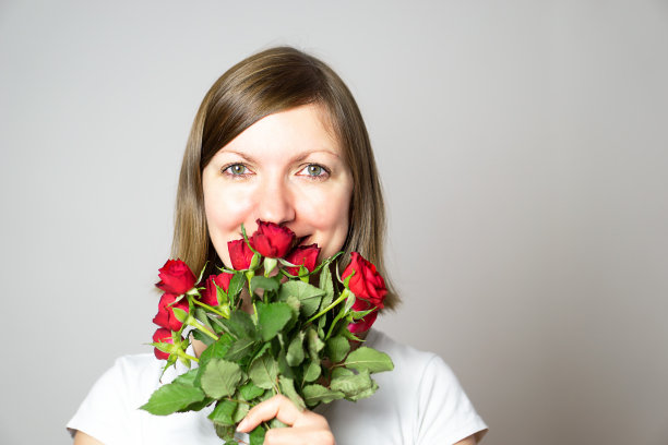 一个微笑的女孩拿着一束红玫瑰的肖像。图片下载