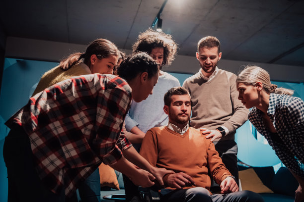 同事们帮助坐在轮椅上的朋友，帮助他在重病后迈出现代办公室的第一步图片下载