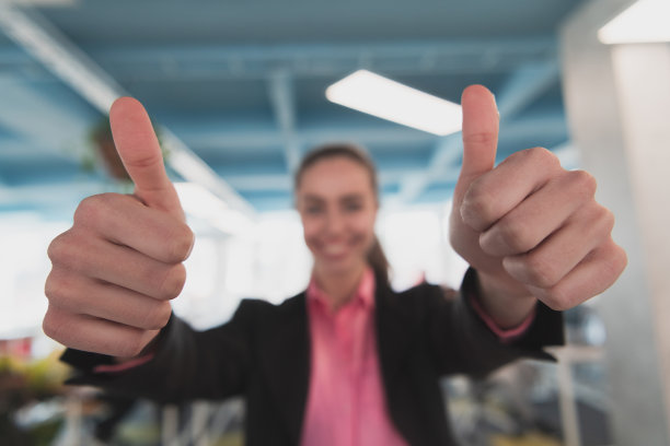 美丽开朗的女商人在创意开放空间的联合办公办公室展示双大拇指广告图片下载