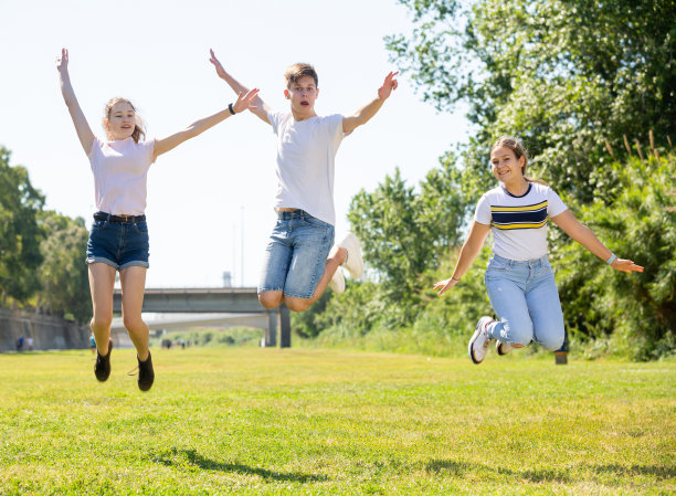 快乐的青少年在绿色的草坪上跳跃图片下载