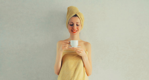 早晨，幸福微笑的女人拿着一杯咖啡，用毛巾裹在头上，擦干她湿漉漉的头发图片下载