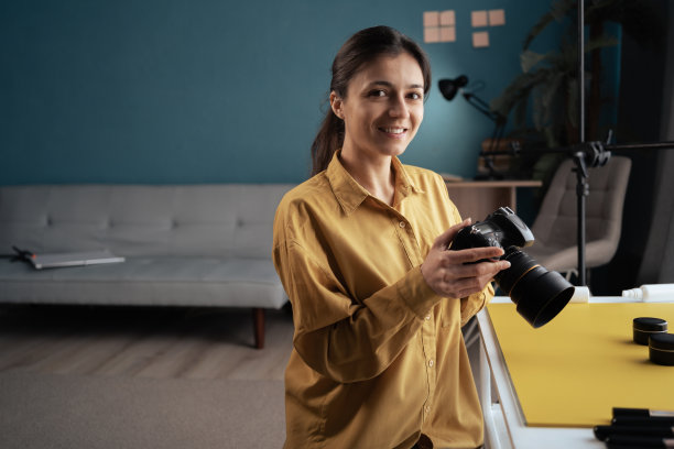 在家庭照相馆里，一位手持相机的专业摄影师微笑着对着相机摆姿势。拍照的女士。摄影。文字空间图片下载