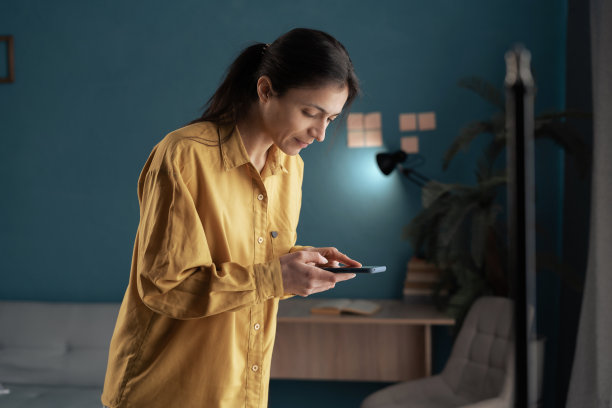 摄影师博客的概念。女人拿着手机在家庭工作室拍照。图片下载