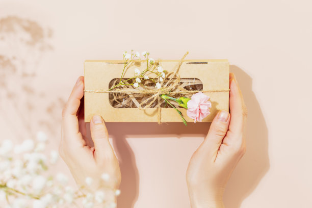 女性手拿工艺礼盒与温柔的花朵在粉红色的背景图片下载