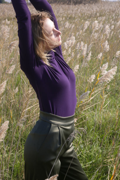 一组穿着紫色高领毛衣和绿色裤子的女模特在草地上摆姿势的照片。户外时尚写真配自然光。图片下载