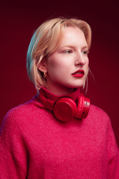 一个美丽的金发女人站在紫红色的背景上，闭着眼睛，脖子上戴着耳机。品红万岁，今年的流行色。图片下载