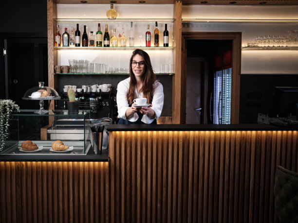 一个咖啡师站在咖啡馆的柜台前，手里拿着一杯新鲜的咖啡。图片下载