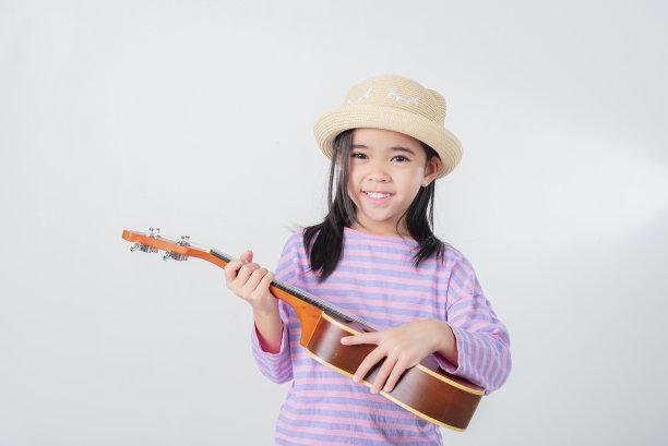 穿着泳装弹尤克里里的可爱小女孩。快乐假期概念。图片下载