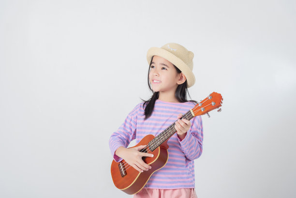 穿着泳装弹尤克里里的可爱小女孩。快乐假期概念。图片下载