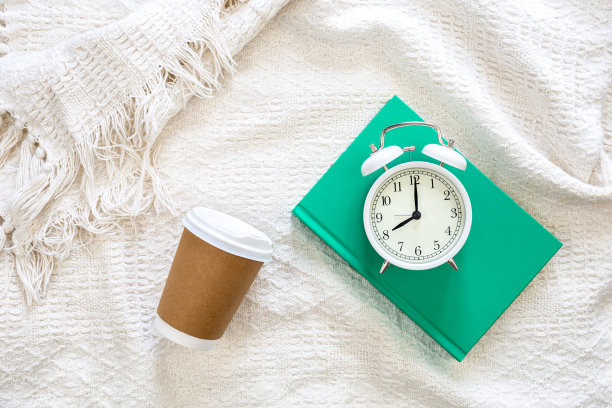 白色的闹钟，一次性纸杯和绿色的书在白色的床上，俯视图。图片下载