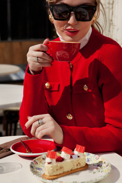 红指甲的时髦女人喝着卡布奇诺咖啡，在咖啡馆吃蛋糕。优雅的女孩端着一杯咖啡，穿着红色运动夹克图片下载