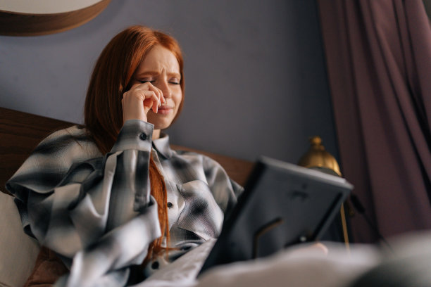 悲痛欲绝的年轻女子躺在床上，拿着相框里的照片哭泣，用爱抚摸着照片，用手帕擦去眼泪。图片下载