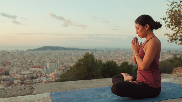 黎明时分，身穿紧身衣的年轻女子在观景处练习瑜伽。女孩在莲花坐姿时举起双手图片下载