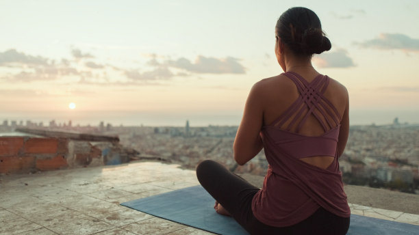 穿着紧身衣的年轻女子在日出时练习瑜伽。后视图图片下载
