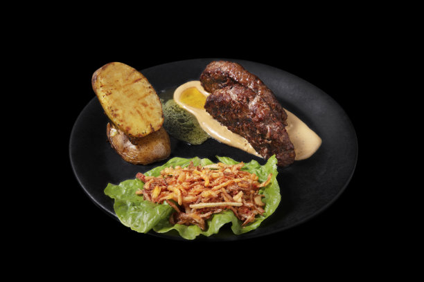 切片肉片配黄油和酱汁，油炸土豆，红薯和沙拉放在盘子里，黑色背景图片下载