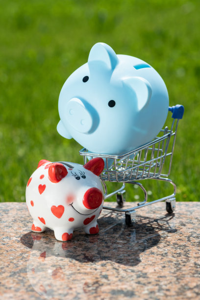 一个蓝色的小猪储蓄罐躺在超市的微型购物车里，背景是绿色的草地图片下载