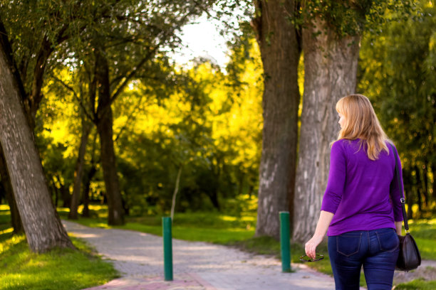 快乐的女人对着夕阳在大自然的夏天回头看。一个年轻女子的剪影望着远处的绿色公园。在夏日公园散步。副本的空间。焦距不清图片下载