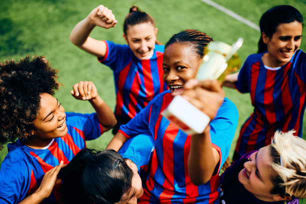 一名黑人足球运动员在体育场被队友抬着，手里拿着夺冠奖杯。图片下载