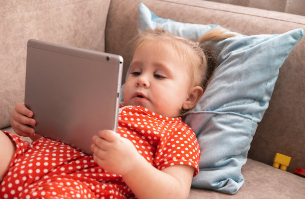 可爱有趣的小女孩躺在沙发上，在平板电脑上看动画片。图片下载