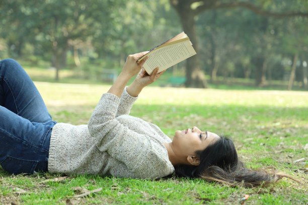 快乐的印度女孩躺在草地上看书图片下载