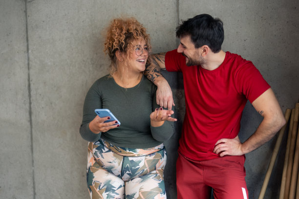 快乐活泼的夫妇在健身房里靠墙站着聊天，锻炼休息图片下载