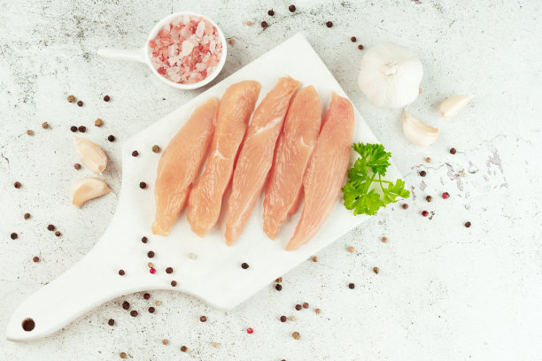 生的新鲜鸡肉片在灰色的背景和新鲜的香草。副本的空间。零售食品。有机食品，健康饮食。食品的概念。前视图。鸡胸片。关闭了。生鸡肉。图片下载