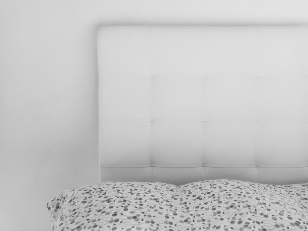 柔软的床头板。真皮或人造革及绗缝织物制成的家具内饰。柔软的床头板靠在浅色的墙上。黑白单色照片图片下载