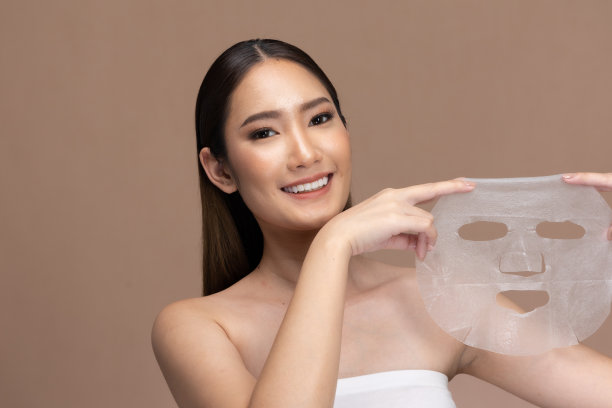 在奶油色的背景下，脸上带着净化面膜的女人。将棉质保湿面膜敷于面部，呵护肌肤。图片下载