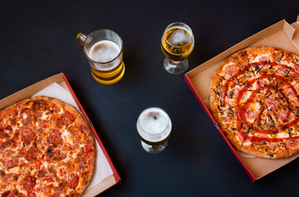 啤酒和新鲜出炉的披萨装在黑色背景的盒子里。图片下载