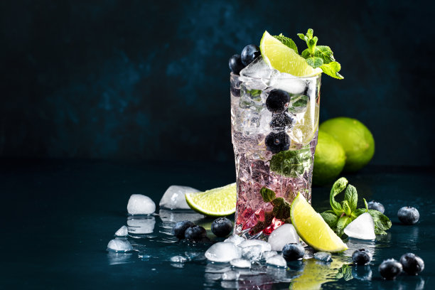 蓝莓莫吉托经典酒精鸡尾酒饮料与酸橙，白朗姆酒，苏打水，蔗糖，薄荷，和冰在深蓝色背景的高球杯。夏日清凉饮料图片下载