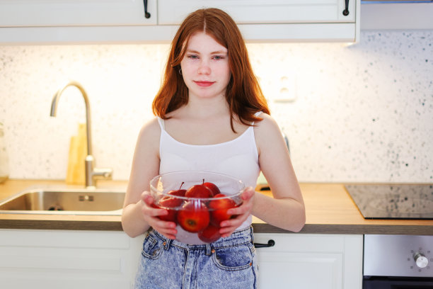 厨房里有个红头发的女孩，手里拿着一个红苹果。高质量照片图片下载