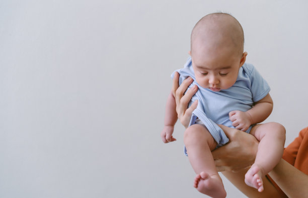 一名亚洲母亲双手抱着可爱的小婴儿睡在灰色的墙上。保健亲情共爱。享受温馨的家庭时刻，母性，育儿理念。图片下载