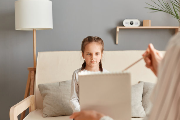 儿童心理诊断的现代方法。女心理学家在办公室检查心理健康，给小女孩病人看照片。图片下载