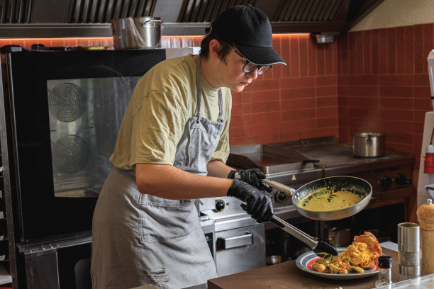 专业厨师在餐厅为顾客上菜前将煎锅里的菜放入盘中图片下载
