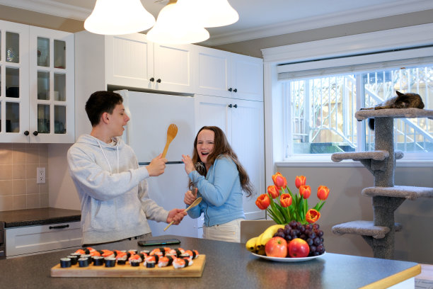 保护你自己。兴奋的男孩和女孩愚蠢地模仿在现代厨房里与厨房用具战斗。有趣的青少年在玩木制刮刀和搅拌器图片下载