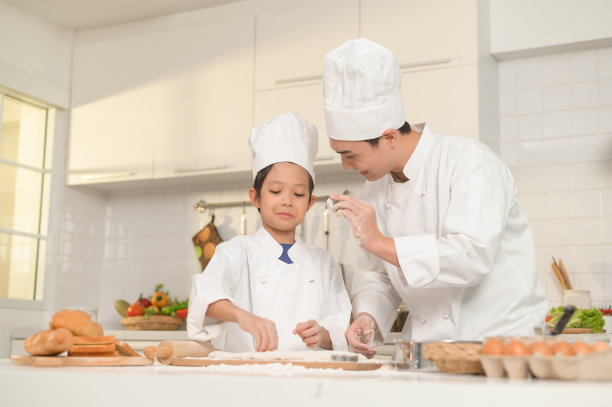 年轻的亚洲父亲和他的儿子穿着厨师制服在家里的厨房里一起烘焙图片下载