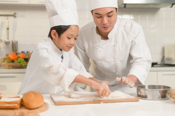 年轻的亚洲父亲和他的儿子穿着厨师制服在家里的厨房里一起烘焙图片下载