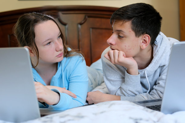 青少年脸上的粉刺男孩和女孩朋友电脑躺在肚子上学习男孩在脸颊上很多青少年皮疹女孩正在仔细看解决问题，找出它是什么图片下载