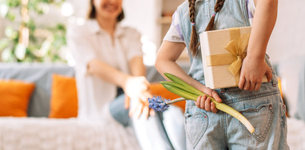 一个孩子背着礼物和鲜花站在妈妈面前，母亲节到了图片下载