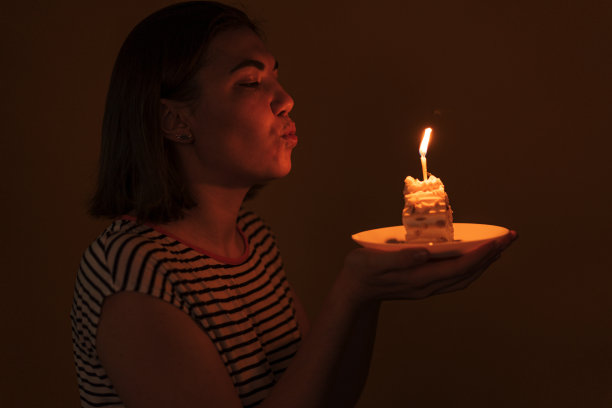一位女士在黑暗的房间里吹灭了一块蛋糕上的蜡烛图片下载