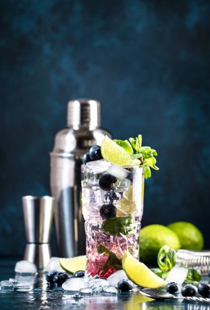 蓝莓莫吉托经典酒精鸡尾酒饮料与酸橙，白朗姆酒，苏打水，蔗糖，薄荷，和冰在深蓝色背景的高球杯。夏日清凉饮料图片下载
