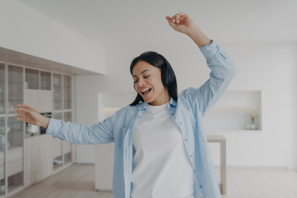 兴奋的女孩戴着无线耳机在家里听音乐，唱歌跳舞。图片下载