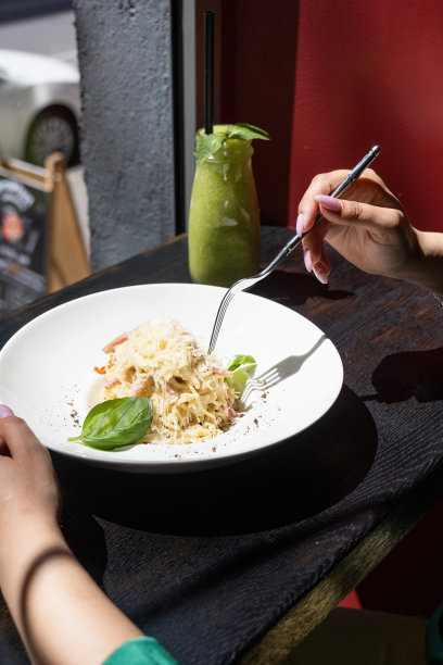 一个女人坐在咖啡馆柜台边吃意大利面，看着窗户，吃着午餐图片下载