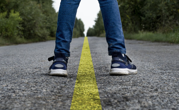 一个穿着牛仔裤和运动鞋的男人的腿站在有分隔条的柏油路上图片下载