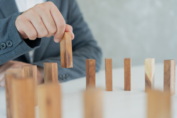 保险用手保护多米诺骨牌。商人的手阻止多米诺骨牌在商业危机中倒下。经营风险的控制和防范经营保险业务的规划与策略。图片下载