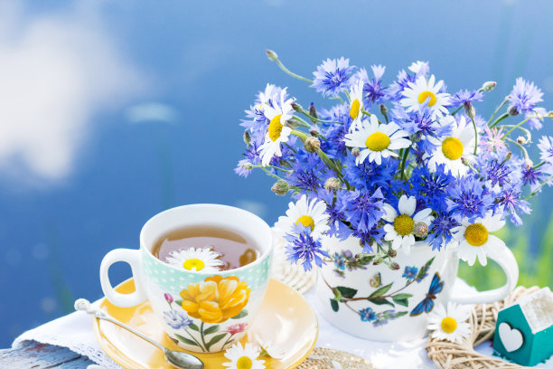 户外以蓝天白云为背景，以鲜花装饰的茶杯装花草茶，健康的蜂蜜花草饮料图片下载