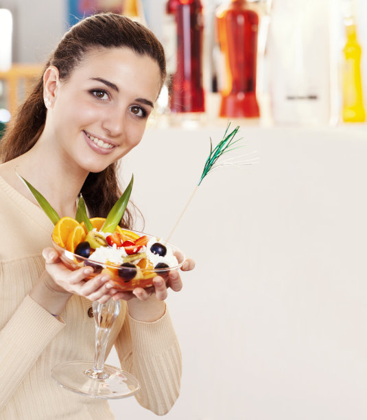 在咖啡馆，咖啡厅，冰淇淋店和糕点店，一个年轻漂亮的微笑着的女人端着一杯水果沙拉，上面放着冰淇淋。黑发女孩笑着看着镜头的肖像图片下载