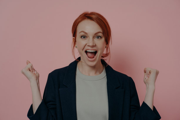 工作室的肖像，喜出望外的红发女商人庆祝成功在粉红色的背景图片下载