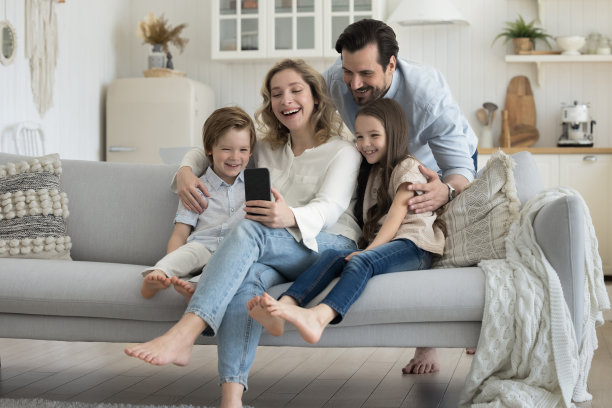 快乐的千禧一代博主父母在沙发上拥抱两个小孩图片下载